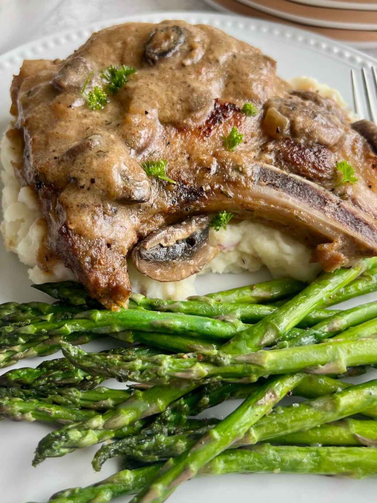 Pork chop on mashed potatoes and a side of asparagus.
