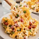 Spoonful of ham and noodle casserole being served on a dish.
