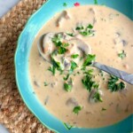 Spoon lifting up hungarian mushroom soup in a blue bowl.