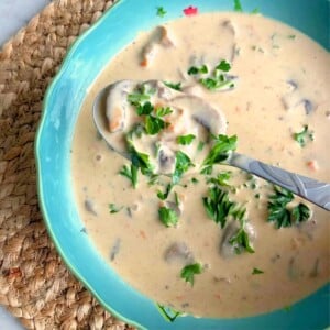 Spoon lifting up hungarian mushroom soup in a blue bowl.