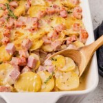 Spoon lifting up scalloped potatoes and ham from dish.