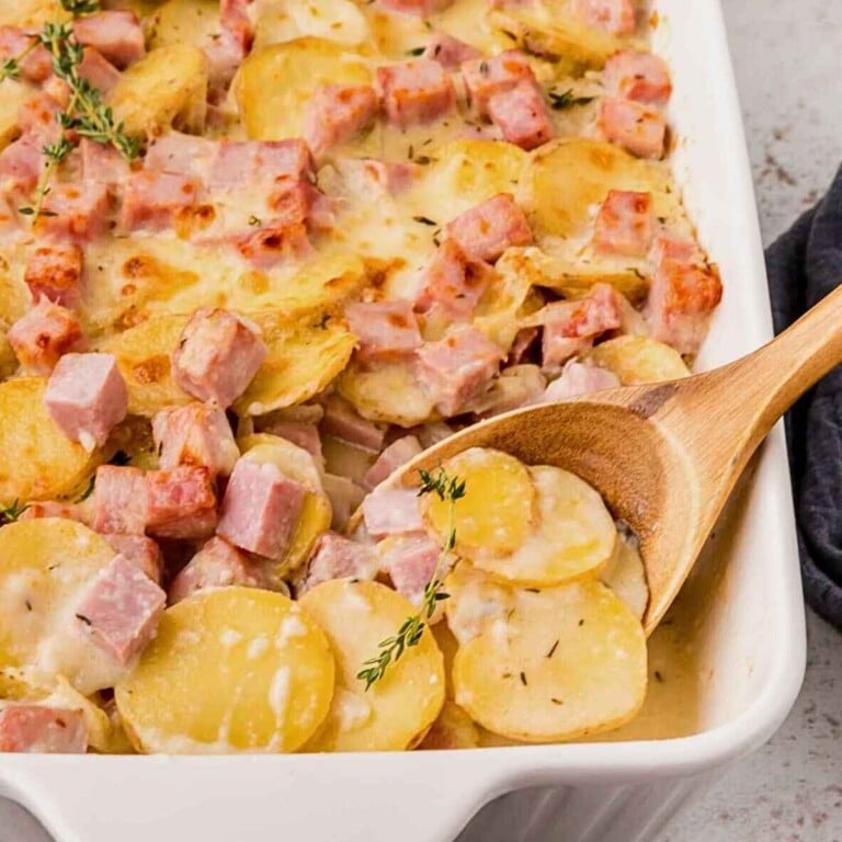 Spoon lifting up scalloped potatoes and ham from dish.