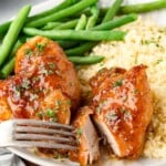 A plate with glazed chicken breast, green beans, and couscous. A fork is cutting into the chicken.
