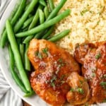 A plate with green beans, couscous, and glazed chicken garnished with herbs.