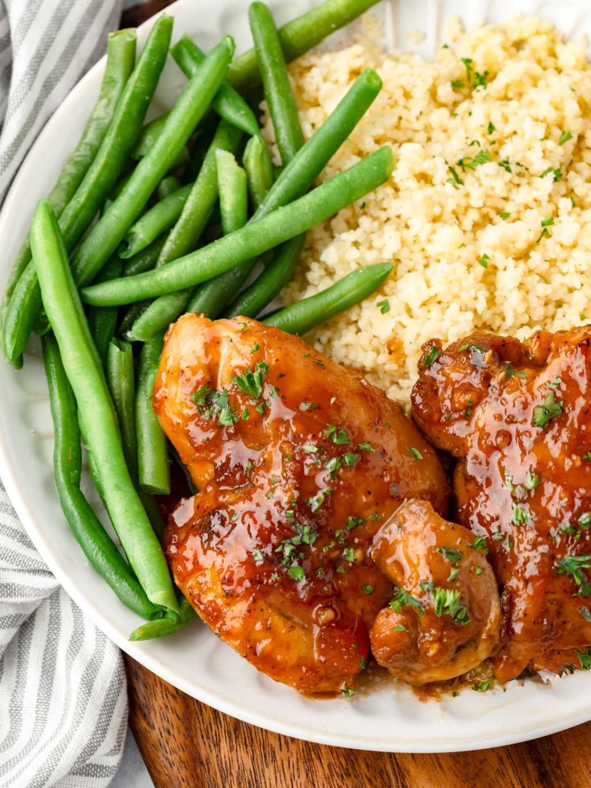 A plate with green beans, couscous, and glazed chicken garnished with herbs.