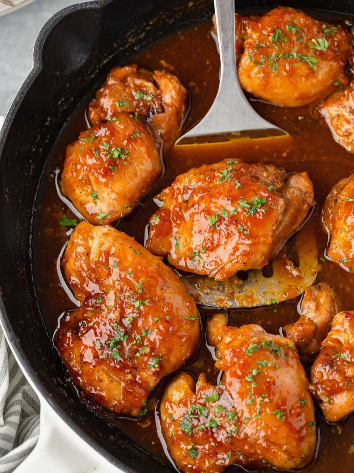 Chicken thighs in a skillet with a glossy brown sauce, garnished with chopped parsley.