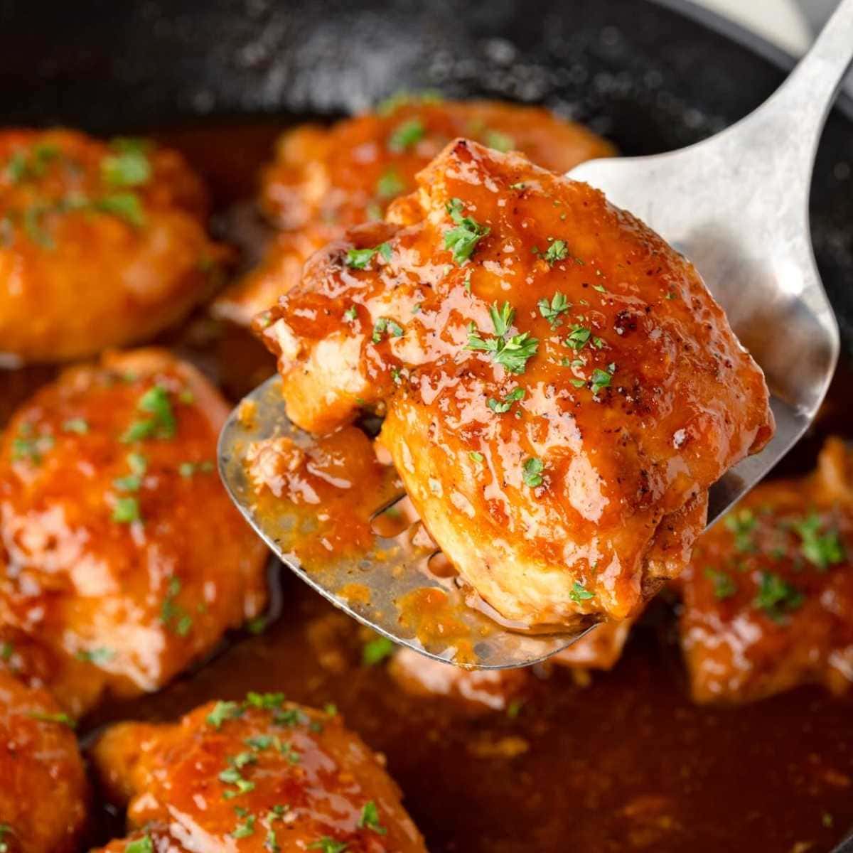 A close-up of glazed chicken pieces in sauce, garnished with chopped herbs, in a skillet.