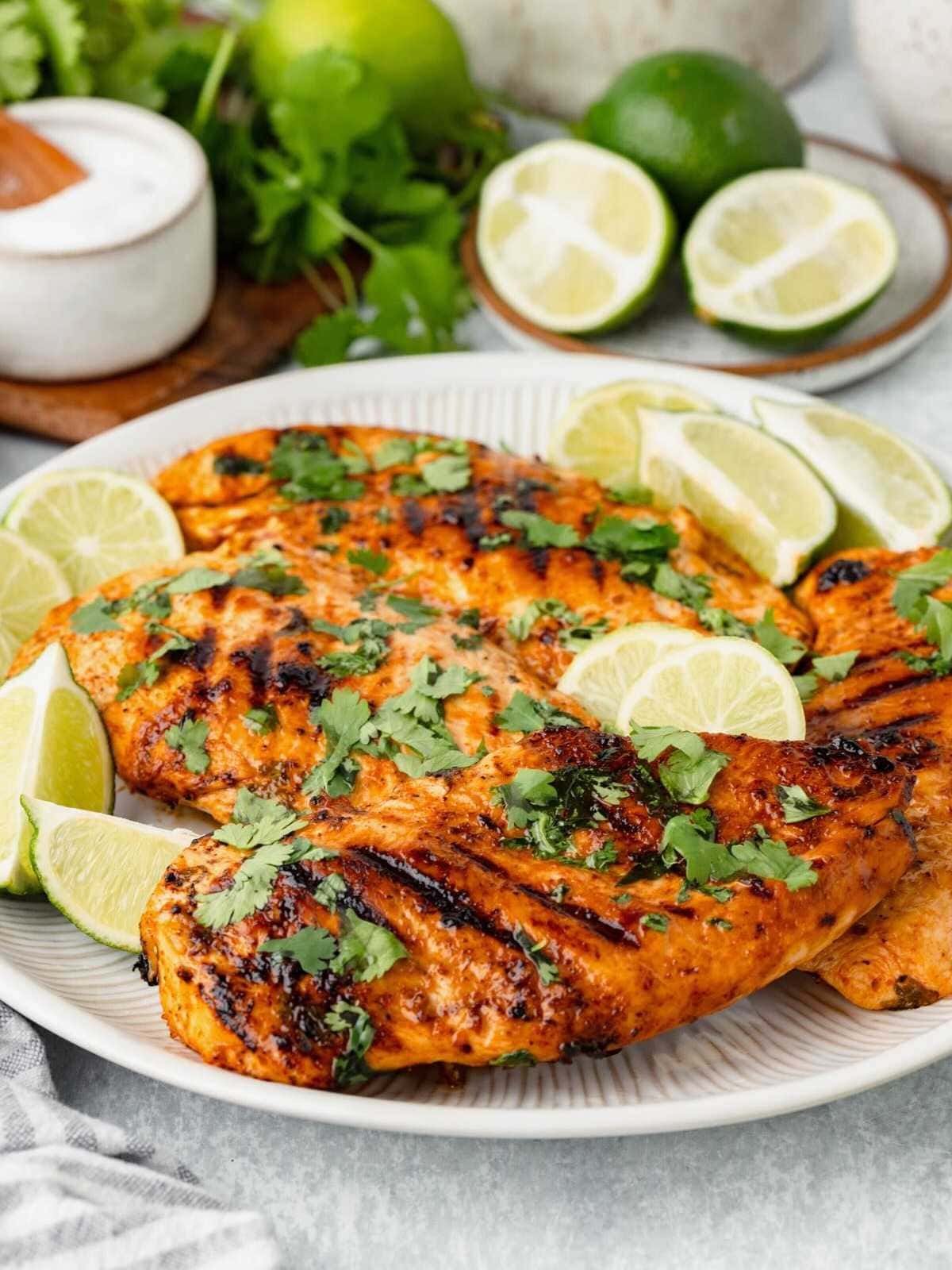 Grilled chicken breast garnished with cilantro and lime wedges on a white plate, with limes in the background.