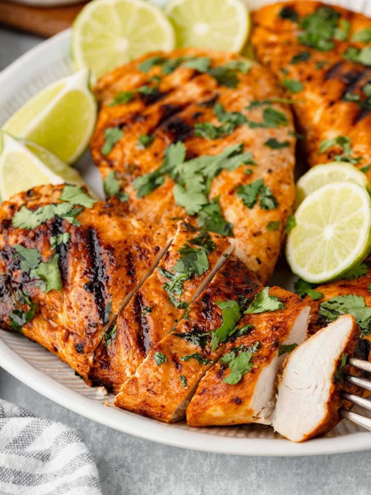 Grilled chicken breasts garnished with cilantro and lime wedges on a plate.
