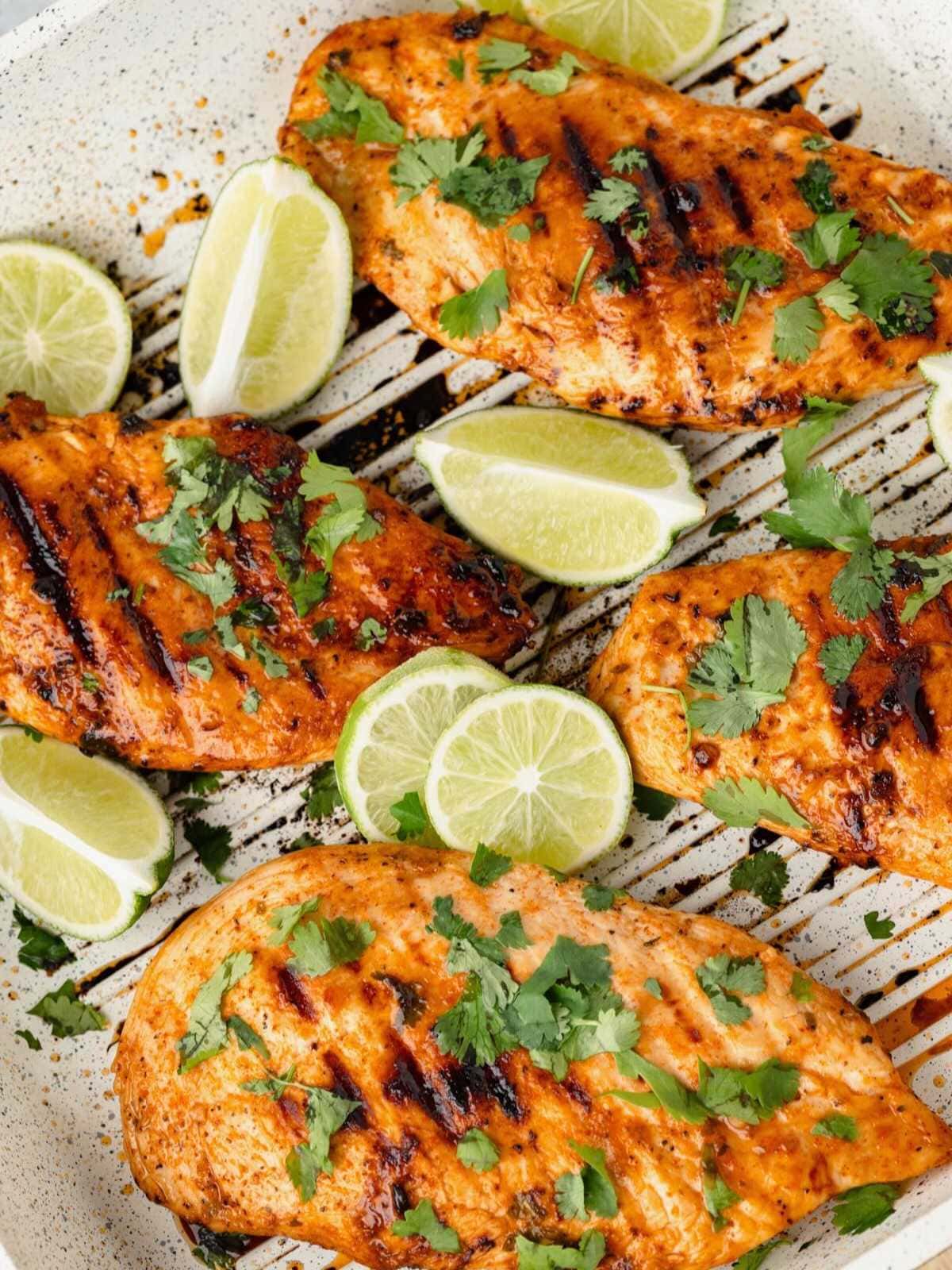 Grilled chicken breasts garnished with cilantro and lime wedges on a white plate.