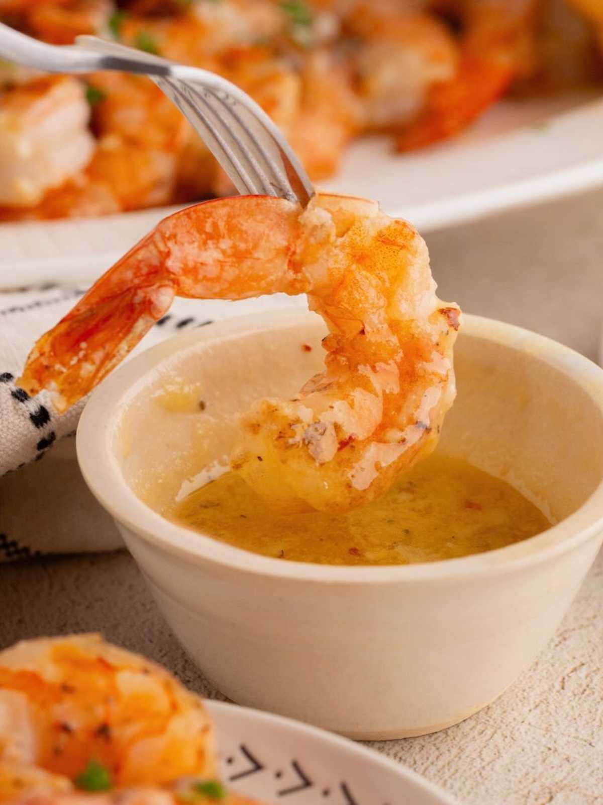 A fork dips a cooked shrimp into a small bowl of melted butter sauce.