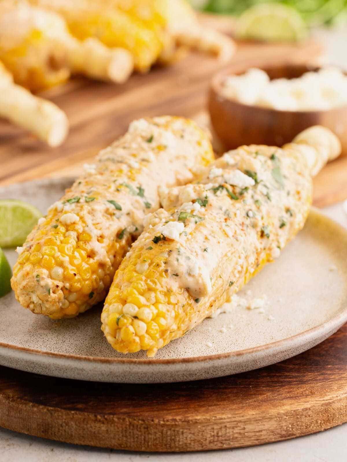 Two grilled corn cobs topped with creamy sauce and herbs on a plate.