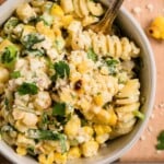 A bowl of creamy pasta salad with corn, cheese, cilantro, and a fork.
