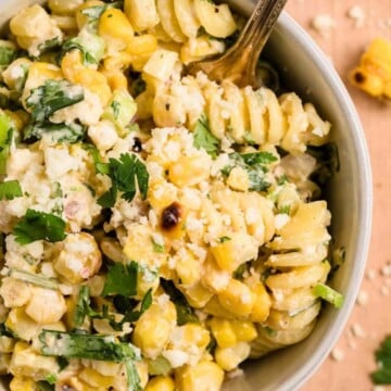 A bowl of Mexican pasta salad with corn, herbs, cheese, and a creamy dressing, with a fork inside.