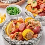 Shrimp boil in foil with shrimp, sausage, corn, and potatoes, garnished with parsley and lemon wedges.