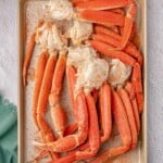 Cooked crab legs seasoned with spices on a baking sheet, placed on a light surface next to a green cloth.