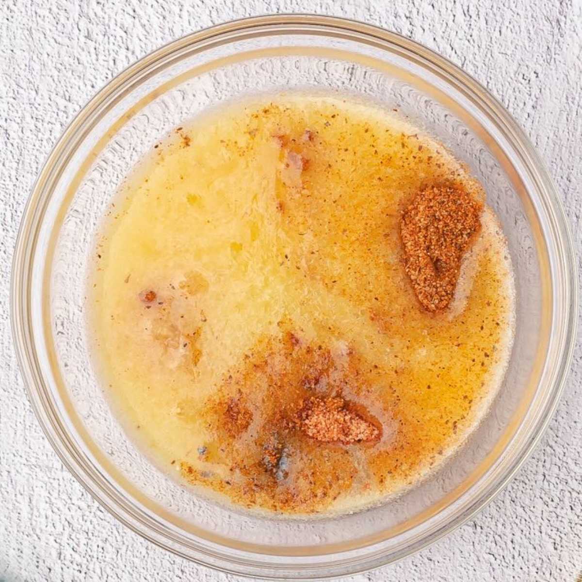 Clear glass bowl with melted butter and brown seasoning.