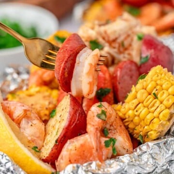 A fork holds shrimp and sausage over a foil packet with corn, potatoes, and shrimp.