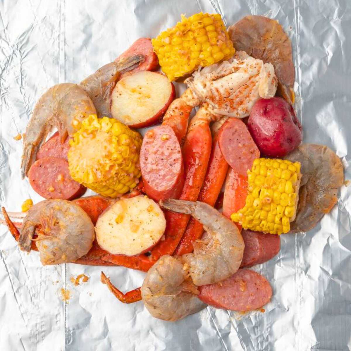 Seafood boil on foil with shrimp, sausage, corn, potatoes, and carrots, ready to be cooked.