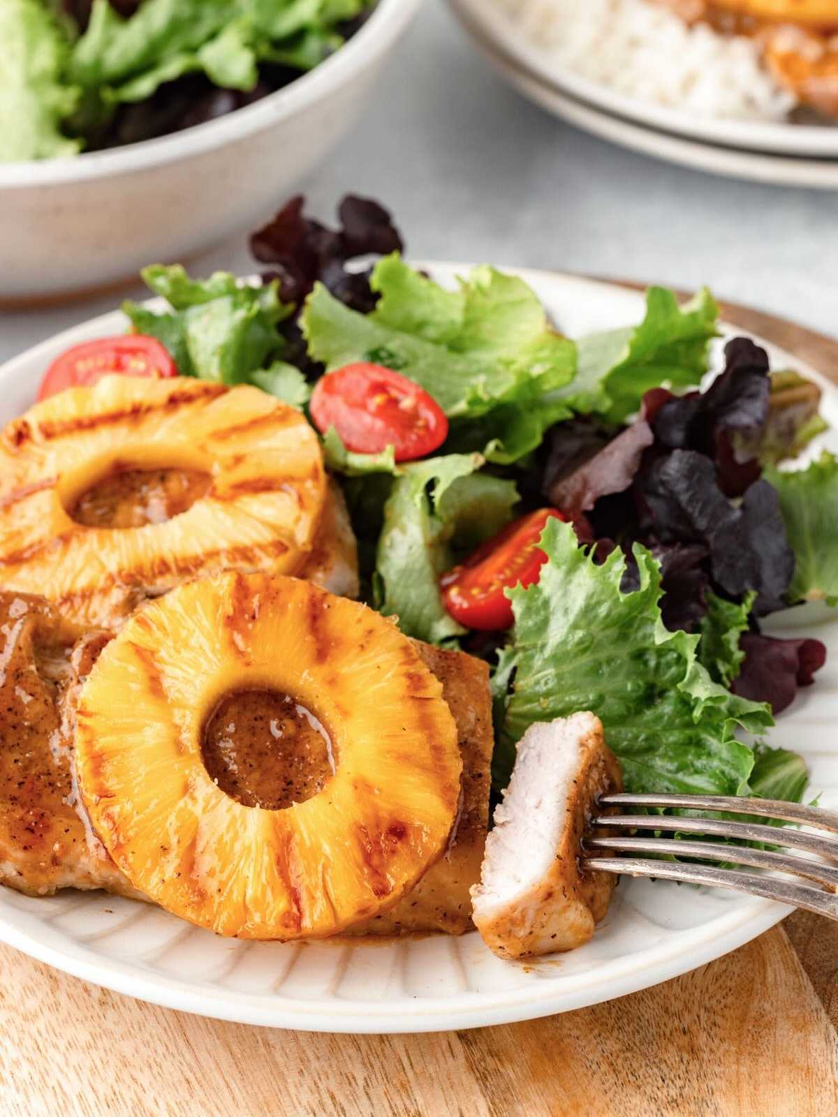 A plate with grilled pineapple rings, meat, and a fresh salad with lettuce and cherry tomatoes.
