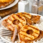 Grilled pork chops topped with pineapple rings served on white rice, with a fork cutting a piece.
