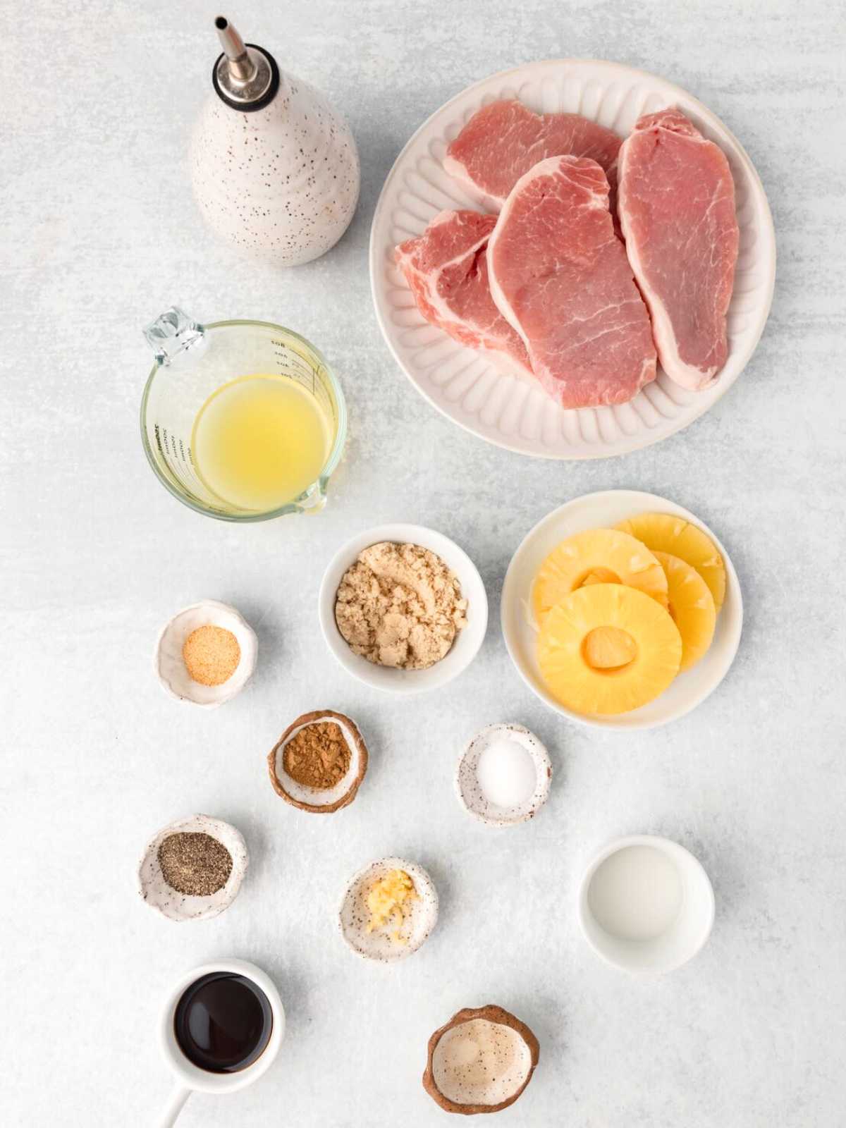 Raw pork chops, pineapple rings, brown sugar, spices, oil, soy sauce, and juice arranged on a light surface.