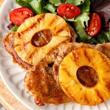 Grilled pineapple pork chops served with mixed greens and cherry tomatoes on a white plate.