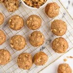 Mini banana nut muffins on a cooling rack with a bowl of chopped walnuts on a marble surface.