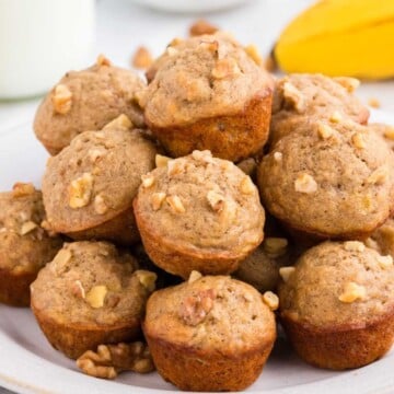 A plate of mini banana nut muffins stacked on top of each other, topped with chopped walnuts.