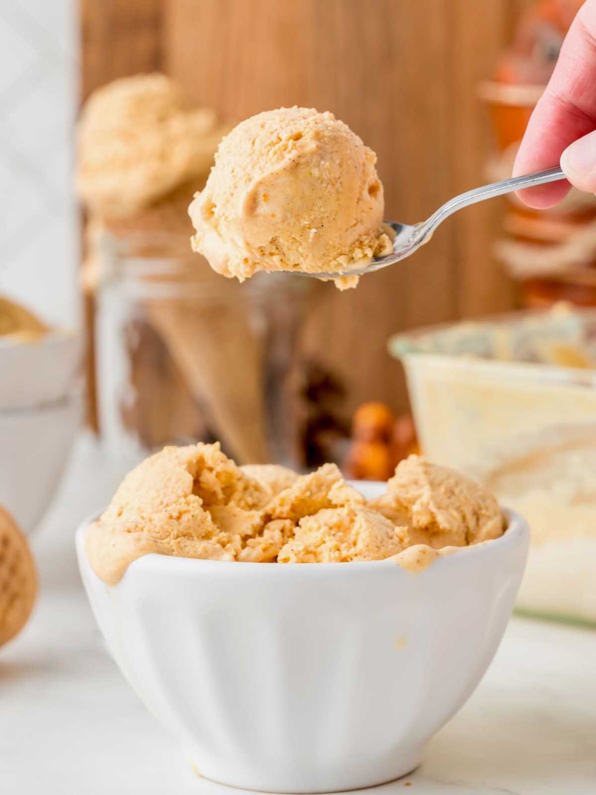 A spoon holds a scoop of creamy ice cream above a white bowl filled with more ice cream.