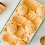 Six scoops of orange-colored ice cream in a glass dish, with a cone and ice cream scoop nearby.