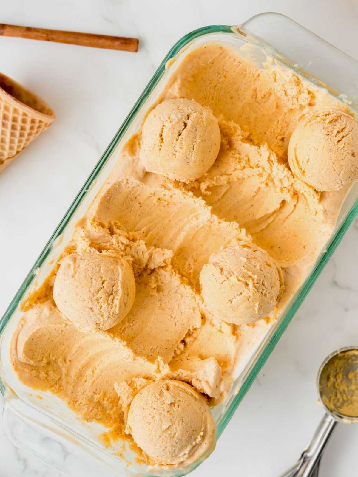Six scoops of orange-colored ice cream in a glass dish, with a cone and ice cream scoop nearby.