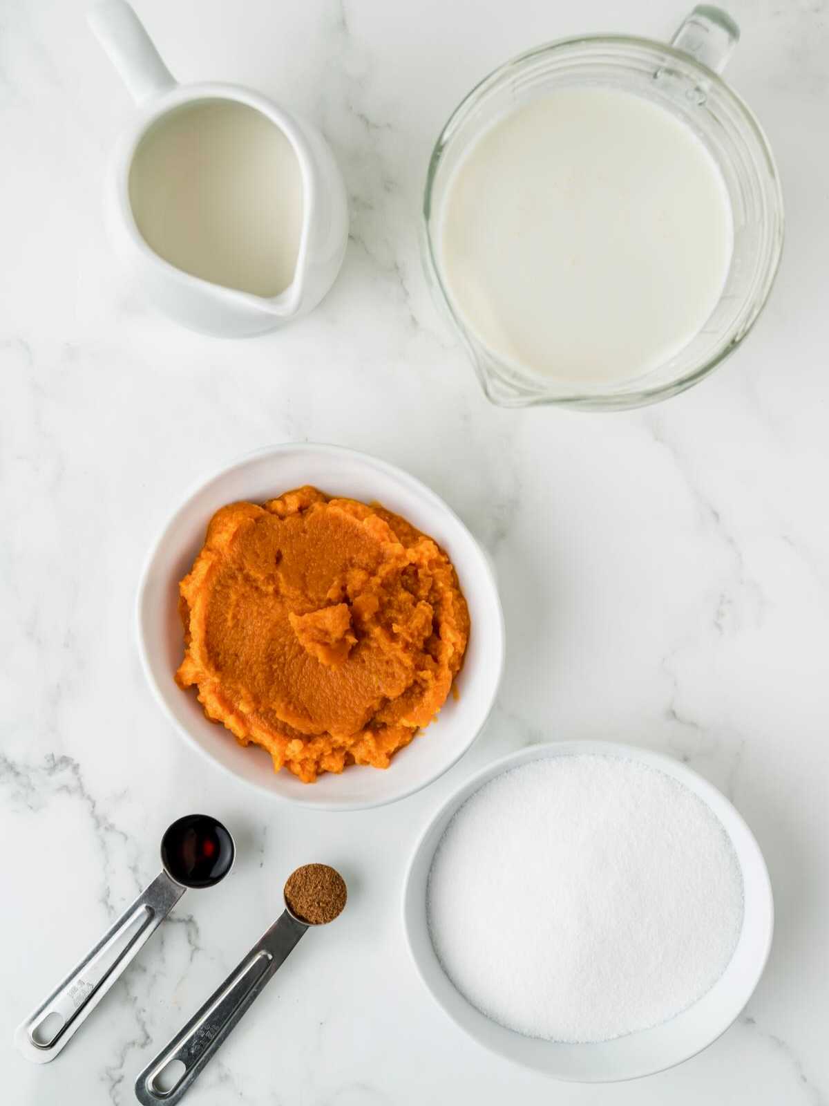 Ingredients on a marble counter: milk, cream, pumpkin puree, sugar, vanilla, and pumpkin pie spice.