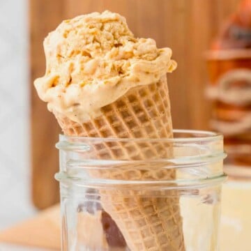 A waffle cone filled with a scoop of creamy ice cream sits inside a clear glass jar.