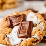 A gooey cookie topped with melted marshmallow and Hersheys chocolate pieces on a white plate.
