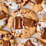 Cookies topped with melted chocolate pieces and gooey marshmallow, arranged closely together.
