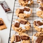 Cookies with melted marshmallow and chocolate pieces cooling on a wire rack, with graham crackers nearby.