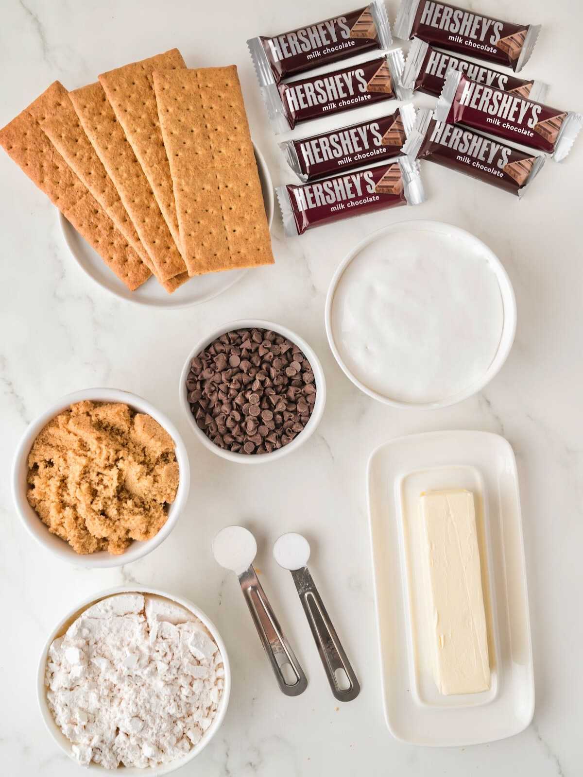 Top view of smores dessert ingredients: graham crackers, Hershey’s bars, butter, sugar, chocolate chips, flour, and brown sugar.