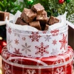 A snowflake tin filled with chocolate fudge sits in front of a decorated Christmas tree.