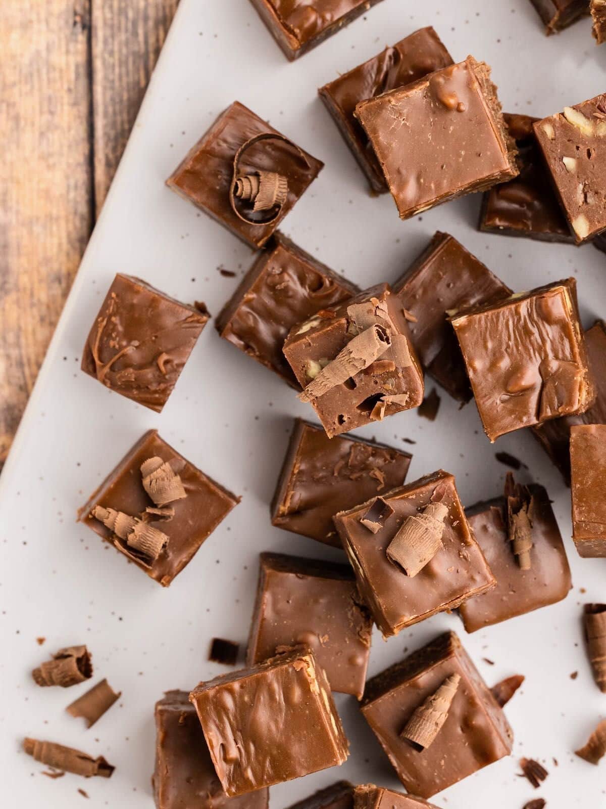 Squares of chocolate fudge with chocolate shavings on a white plate, viewed from above.