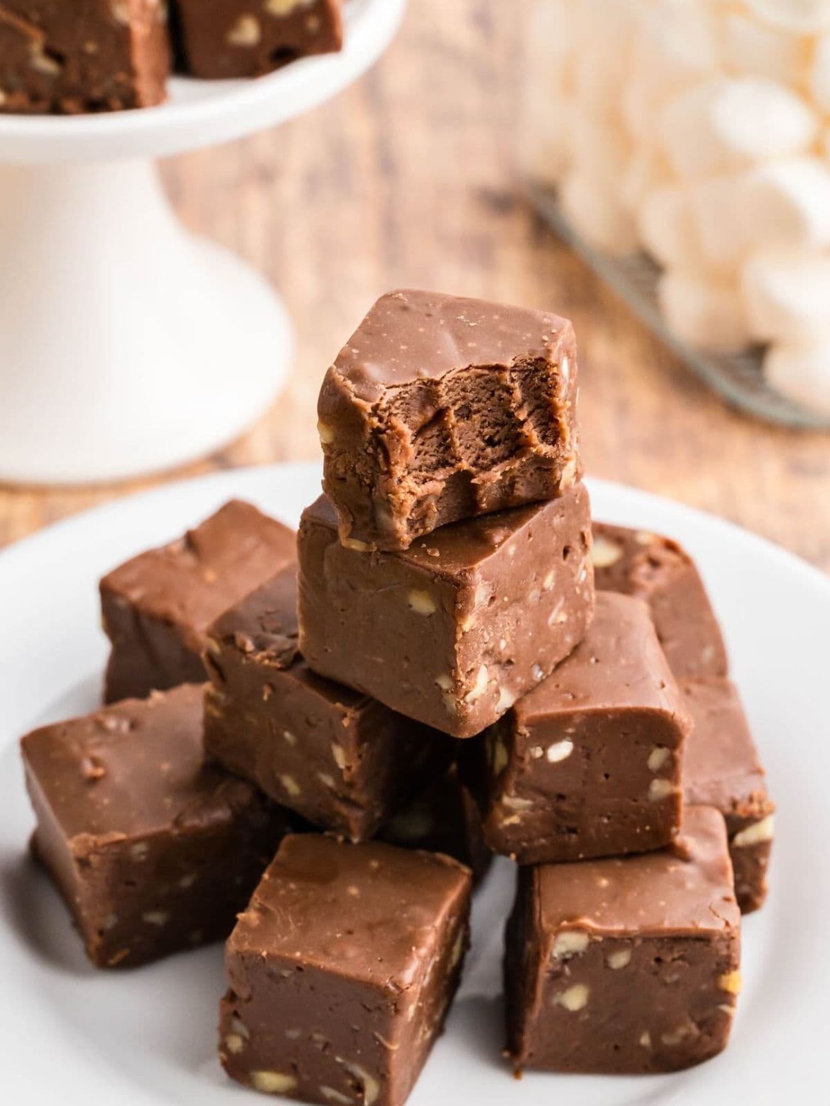 A stack of chocolate fudge squares with nuts, one on top has a bite taken out, on a white plate.