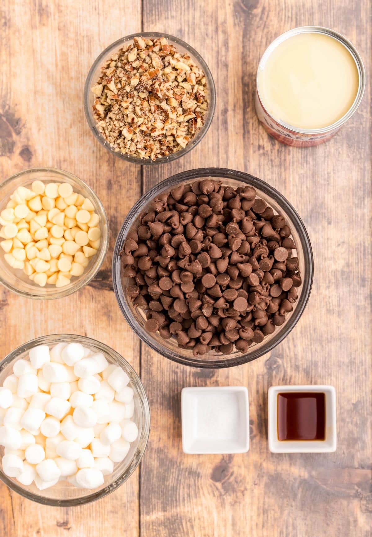 Bowls of chocolate chips, white chips, marshmallows, chopped nuts, salt, vanilla, and sweetened condensed milk.