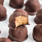 Chocolate-covered peanut butter balls, with one bitten to show the creamy peanut butter filling inside.