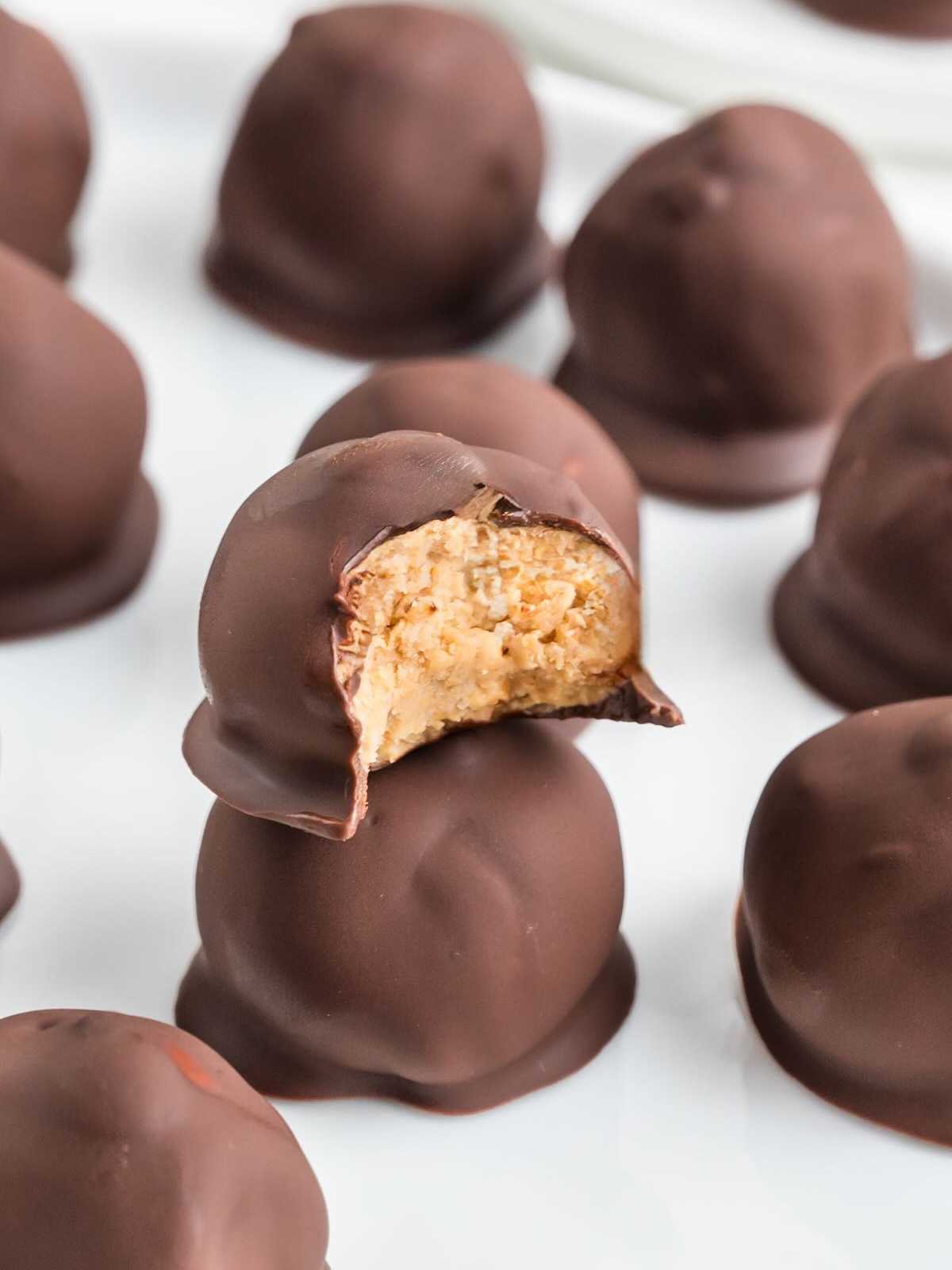 Chocolate-covered peanut butter balls, with one bitten to show the creamy peanut butter filling inside.