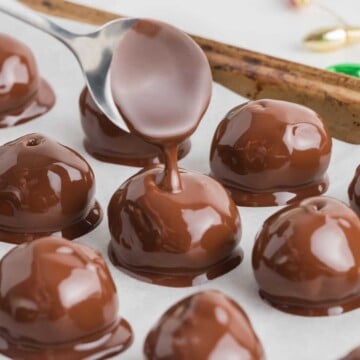 A spoon drizzles melted chocolate over round chocolate-covered peanut butter balls on parchment paper.