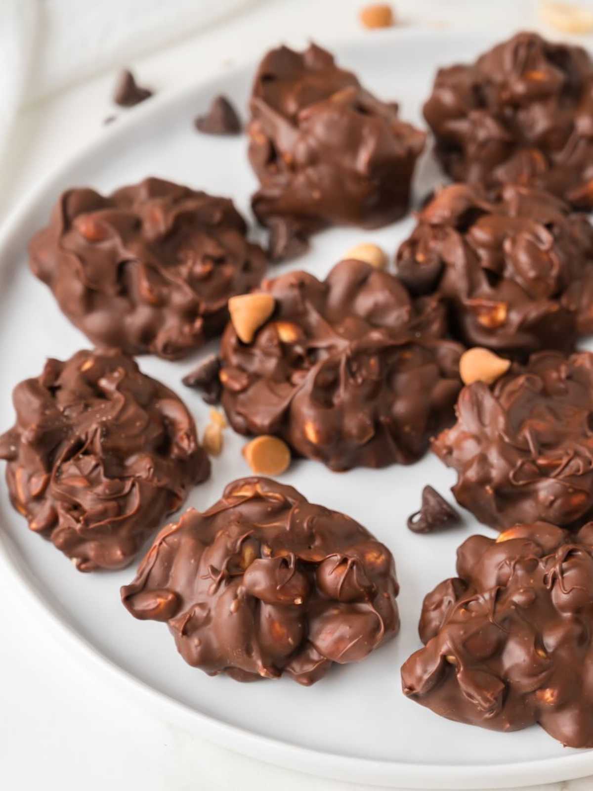 Chocolate clusters with peanuts and butterscotch chips arranged on a white plate.