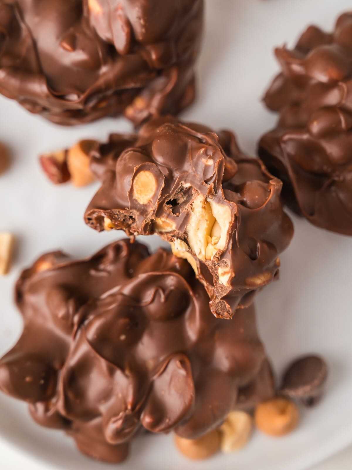 Clusters of chocolate-covered peanuts and candies, with one cluster showing its nutty interior from a bite.