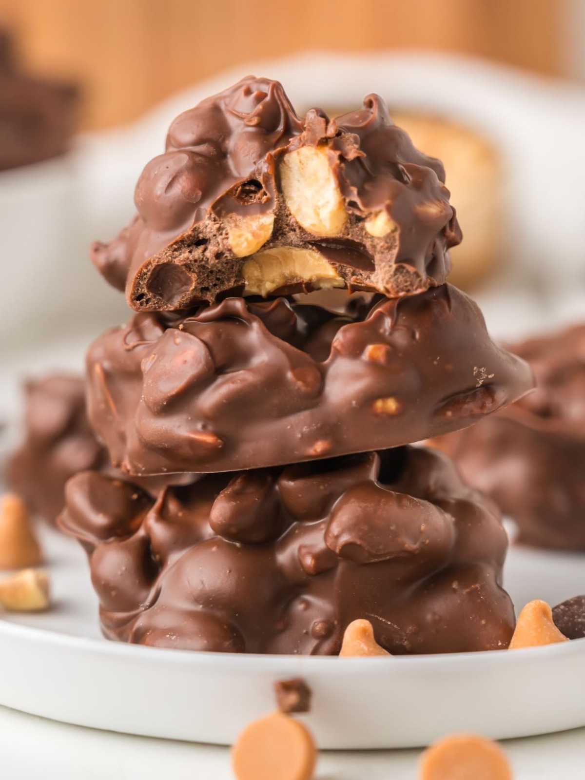 Three chocolate peanut clusters stacked on a plate, with the top one bitten to show the inside.