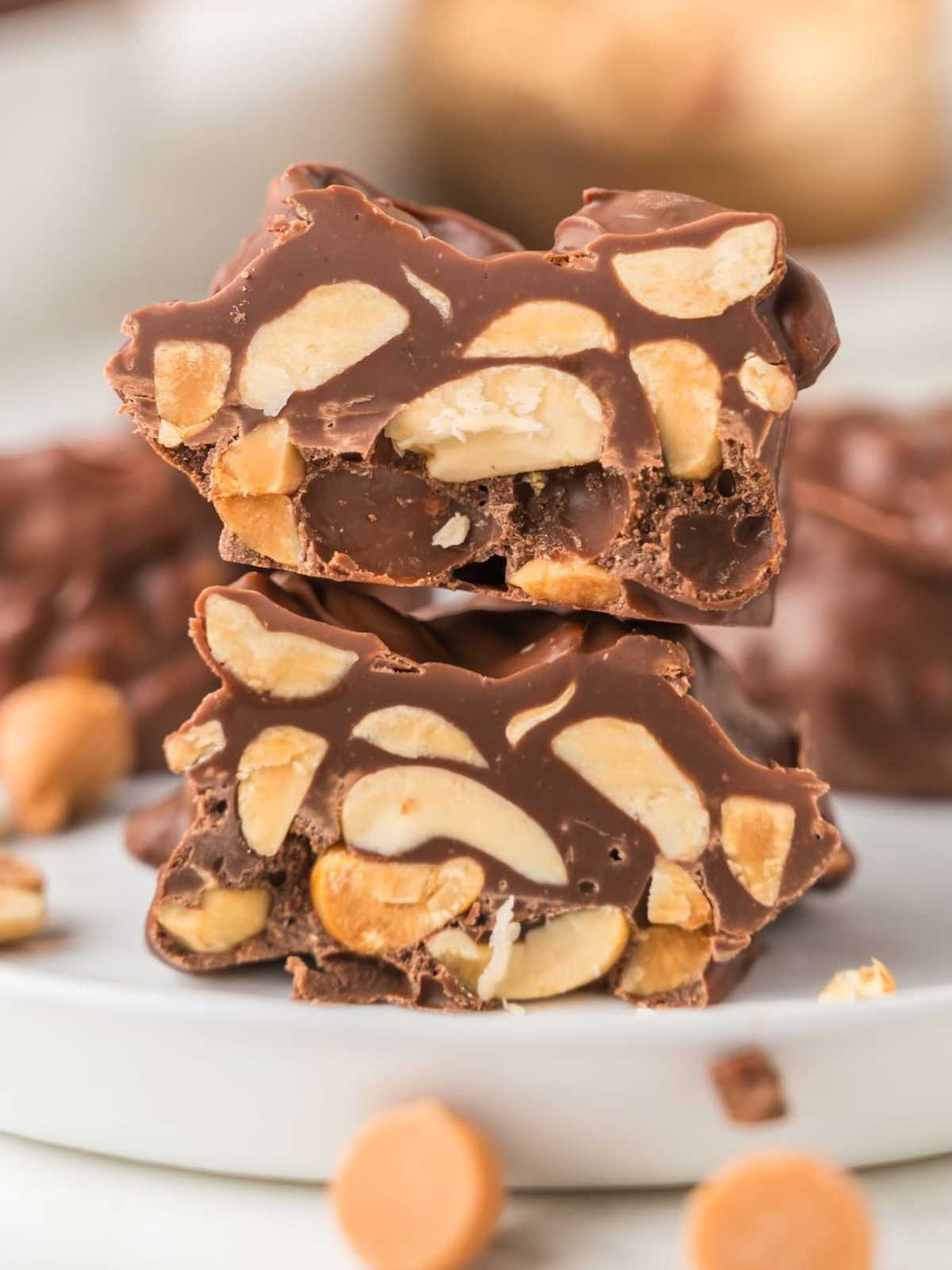 Close-up of chocolate clusters with visible peanuts, stacked on a white plate.