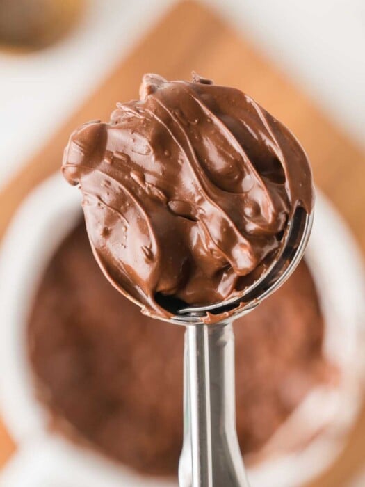 A metal scoop holding a generous serving of creamy chocolate.